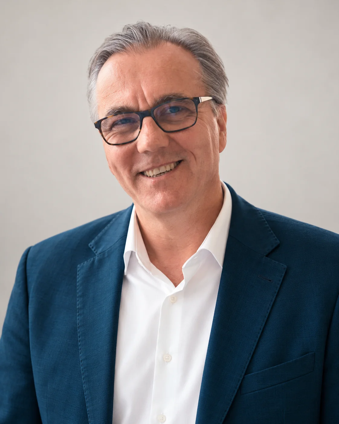 Chris wearing glasses, a blue blazer and a white open-collar shirt, against a light grey background.