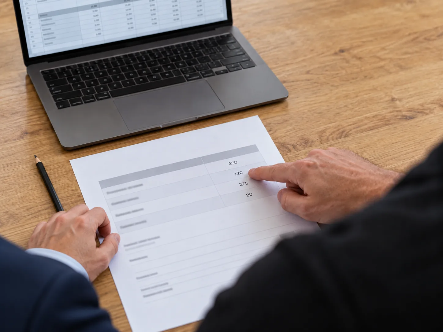 Over-the-shoulder view of two people reviewing an estimate, with a finger pointing to a figure beside an open laptop.